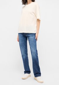 Beige puuvillainen T-paita, jossa on lyhyet hihat ja valkoinen teksti. Yhdistetty sinisiin suoralahkeisiin farkkuihin ja valkoisiin tennareihin. Minimalistinen design.