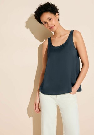 Marineblaue ärmellose Bluse mit rundem Ausschnitt, glatter Textur und lockerer Passform, kombiniert mit weißen weit geschnittenen Hosen.