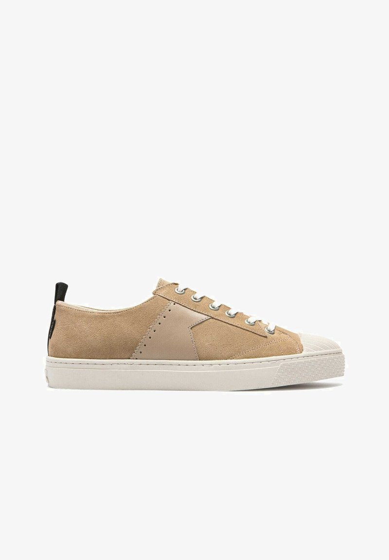 Baskets en suède beige avec des accents en cuir lisse, semelle en caoutchouc blanc et fermeture à lacets grise. Présente un tirant noir à l'arrière.