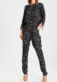 Svart jumpsuit med färgglad blommönster. Har långa ärmar, midja med dragsko och justerbara knyte vid ärmsluten. Slätt tyg och avsmalnande ben.