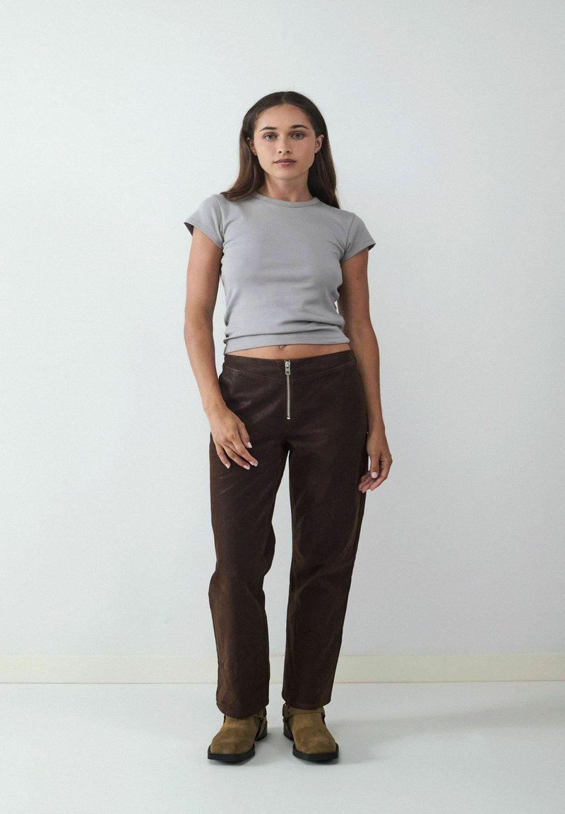 Grijze top met korte mouwen gecombineerd met bruin leren broek met een rits aan de voorkant. De broek heeft een gladde textuur en een getailleerde pasvorm.