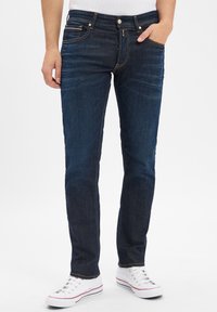 Mörkblå denimjeans med rak passform, med orange sömmar, fem fickor och en klassisk knäppning. Matchas med vita sneakers.