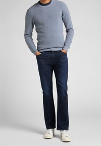 Ljusblå stickad tröja med rundad hals, kombinerad med mörkblå jeans. Vita sneakers fulländar outfiten, som har diskret märkning på tröjan.