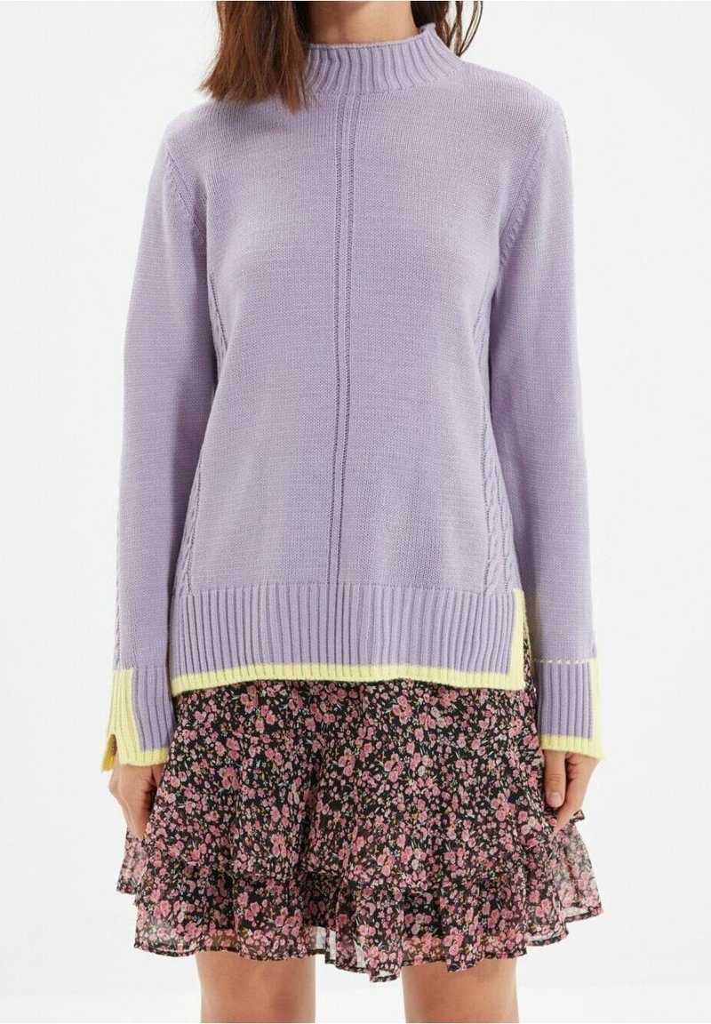 Maglione lavorato a maglia lavanda con colletto e polsini a coste, con accenti gialli sull'orlo. Abbinato a una gonna nera con volant floreale.