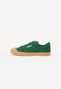 Green canvas sneaker with a gum rubber sole, round toe, flat laces, contrasting stitching, and a small brand label on the side.