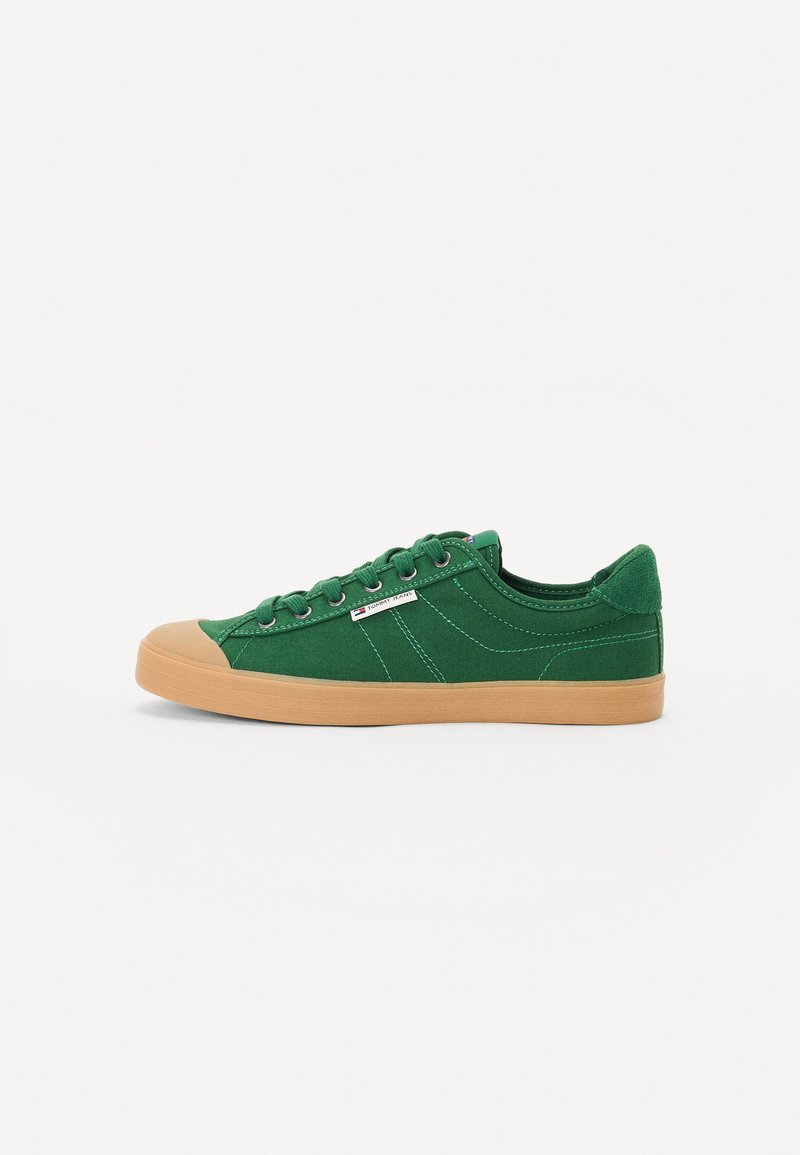 Green canvas sneaker with a gum rubber sole, round toe, flat laces, contrasting stitching, and a small brand label on the side.
