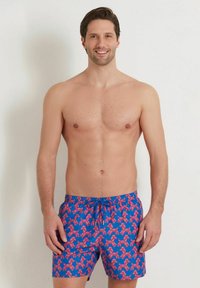 Shorts de bain d'un bleu vif avec un motif de chien en ballon rose. Ils sont dotés d'une taille élastique avec un cordon de serrage pour un ajustement optimal.
