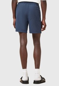 Tummansiniset uimapuvut, joissa on joustava vyötärö, takatasku ja sileä, kevyen tuntuinen kangas, nähtynä takaa.