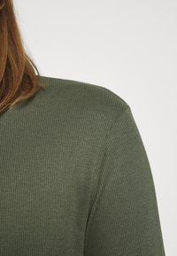 Ribbet langærmet skjorte i olivengrøn, med en struktureret overflade og en afslappet pasform. Udsnittet er crew-type, som viser blødt stof.