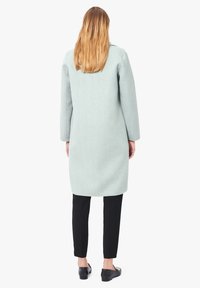 Cappotto in lana verde menta chiaro con taglio dritto, maniche lunghe e orlo di media lunghezza. Abbinato a pantaloni neri aderenti e scarpe basse.