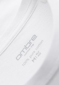 Étiquette à l'intérieur du col d'un T-shirt en coton blanc indiquant la marque "ambre", 100 % coton pur, et la taille M/48 EUR.