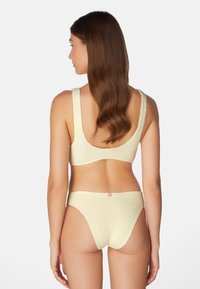 Gul strukturerad bikiniöverdel med breda remmar och matchande lågvärdiga underdel. Bakre vy visar en enkel design och en slät finish.