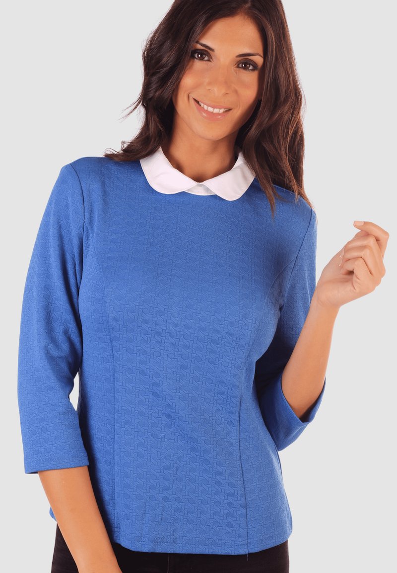 Blusa azul texturizada con un cuello tipo Peter Pan blanco y mangas tres cuartos, que presenta una silueta ajustada y patrones de diseño sutiles.