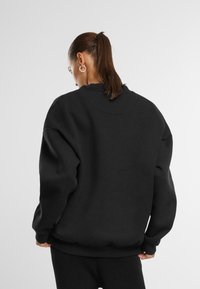 Felpa nera oversize realizzata in tessuto spesso, con colletto e polsini a coste. Presenta spalle abbassate e una vestibilità rilassata.