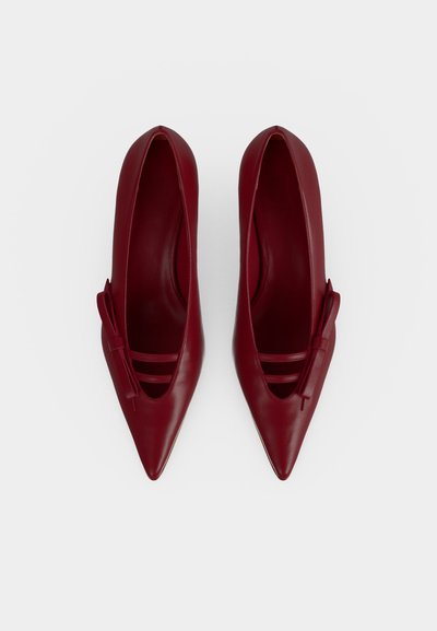Paire de chaussures plates rouges à bouts pointus avec un petit nœud sur le côté, vue de dessus sur fond blanc.