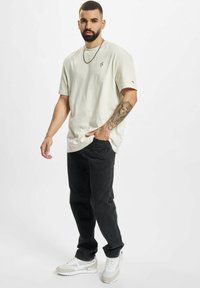 Světle béžové oversized tričko s malým černým logem, spárované s černými džínami a bílými teniskami se světle šedými akcenty.