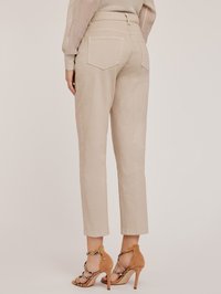 Beżowe dopasowane spodnie o wysokim stanie, z dwoma tylnymi kieszeniami i podwiniętymi nogawkami, zestawione z brązowymi sandałami na obcasie z ozdobnymi akcentami.