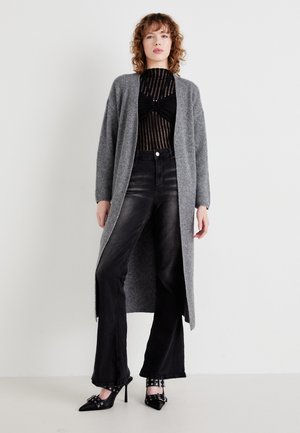 Long cardigan gris en tricot, associé à un body rayé noir, un jean noir taille haute et des escarpins noirs pointus.