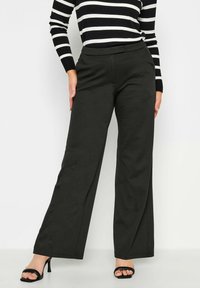 Zwarte, wijde broek van een gladde stof, met een op maat gemaakte taille en minimale stikseldetails. Draag met een zwart-wit gestreepte top.