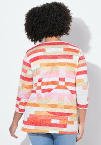 Kevyt, monivärinen pusero, jossa on geometrinen kuvio punaisen, vaaleanpunaisen, oranssin ja beigeen sävyissä; kolme neljäsosaa hihat ja pyöreä kaula-aukko.