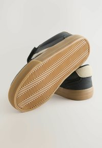 Czarne sneakersy z miękkim beżowym akcentem, z fakturowaną brązową podeszwą gumową o wzorze w jodełkę, zaprojektowane z myślą o komforcie i przyczepności.