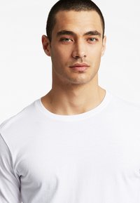 Hvid crew-neck t-shirt med en glat tekstur. Slim fit design, korte ærmer og minimal detalje. Baggrunden er helt hvid.