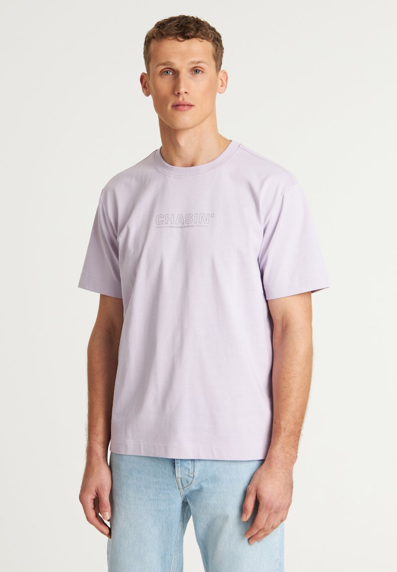 Šviesiai purpurinė trumpomis rankovėmis marškinėliai su apvaliu kaklu ir iškilniu "CHASIN'" logotipu priekyje. Minkšta medžiaga ir laisvas kirpimas.