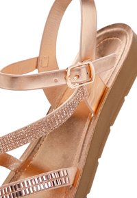 Rose gold sandals with shiny metallic straps, embellished with rhinestones, featuring a chunky wedge sole for added comfort.