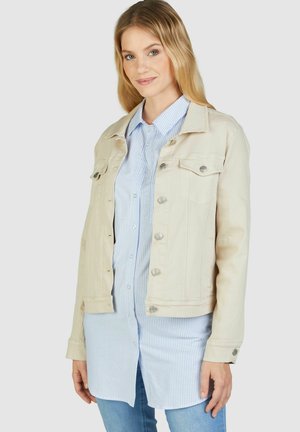Beige denimjack met twee borstzakken, zilveren drukknoopjes en een getailleerd ontwerp, gedragen over een lichtblauw gestreept shirt.