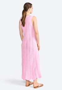 Robe longue sans manches en tricot rose avec un motif en chevron, dotée d'un ourlet en dents de scie. Portée avec des sandales plates, mettant en valeur une coupe décontractée.