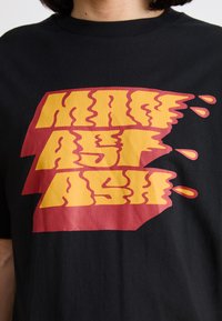 Black cotton t-shirt featuring bold, wavy yellow and red graphic text, with a textured look and drips.