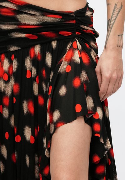 Czarna spódnica z tkaniny, ozdobiona czerwonymi i beżowymi kropkami, z marszczonym pasem i bocznym rozcięciem dla swobody ruchu i stylu.