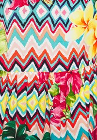 Blommönstrad tyg med livliga sicksackränder i röd, blå, gul och grön med olika tropiska blommor och blad.