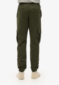 Pantalones de chándal cargo en verde oliva con cintura elástica, bolsillos laterales y puños elásticos. Fabricados con una suave mezcla de algodón para mayor comodidad.