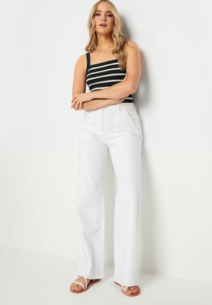 Débardeur rayé noir et blanc avec fines bretelles, associé à un pantalon large taille haute blanc et des sandales plates blanches. Tissu lisse.