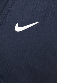 Logo blanc Nike Swoosh sur un tissu de sport texturé bleu foncé avec des coutures visibles le long des bords.