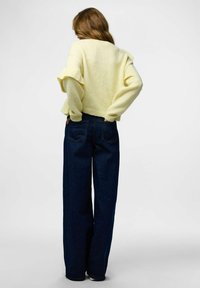 Żółty sweter z dzianiny z falbankami na rękawach, zestawiony z ciemnoniebieskimi szerokimi spodniami dżinsowymi. Sweter ma krótki krój; spodnie mają tylne kieszenie.