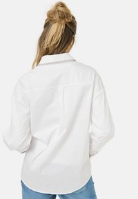 Camicia bianca con bottoni, a maniche lunghe e colletto standard, dotata di yoke posteriore e spacchi laterali per un fit rilassato.