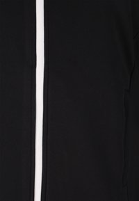 Zwarte kleding met een ritssluiting aan de voorkant en een opvallende witte streep. Gemaakt van een zachte stof met een gladde textuur.