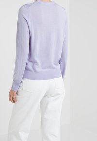 Pull en maille violet clair à manches longues, col rond et ourlet côtelé. Assorti à un pantalon blanc taille haute, mettant en valeur une texture douce.