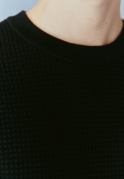 Pulover negru cu textură, având un guler cu nervuri și un model în formă de grilă, care evidențiază o prezentare detaliată a țesăturii și a texturii.