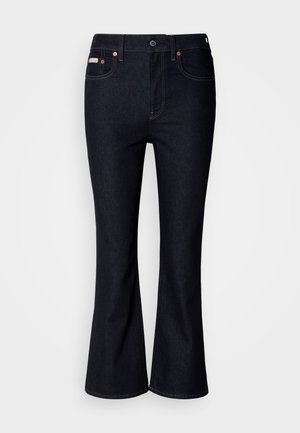 Tamsiai mėlyni platėjančių kojų džinsai iš džinso audinio, turi klasikinį penkių kišenių dizainą, metalinę mygtuko užsegimą ir kontrastingas siūles.