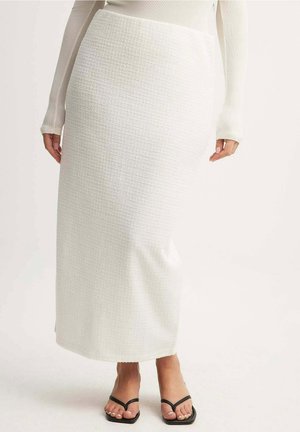 Biała, teksturowana maxi spódnica z dopasowanym pasem. Stylizowana z czarnymi sandałami na cienkich paskach. Gładki materiał i prosta sylwetka.