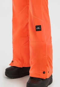 Oranje sneeuwbroek van waterdicht materiaal, met versterkte stiksels, een zijlogo-patch en verstelbare enkelsluitingen.