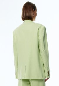 Lichtgroene blazer met een relaxte pasvorm, enkele vent aan de achterkant en knoopmanchetten. Soepele textuur en minimalistisch ontwerp.