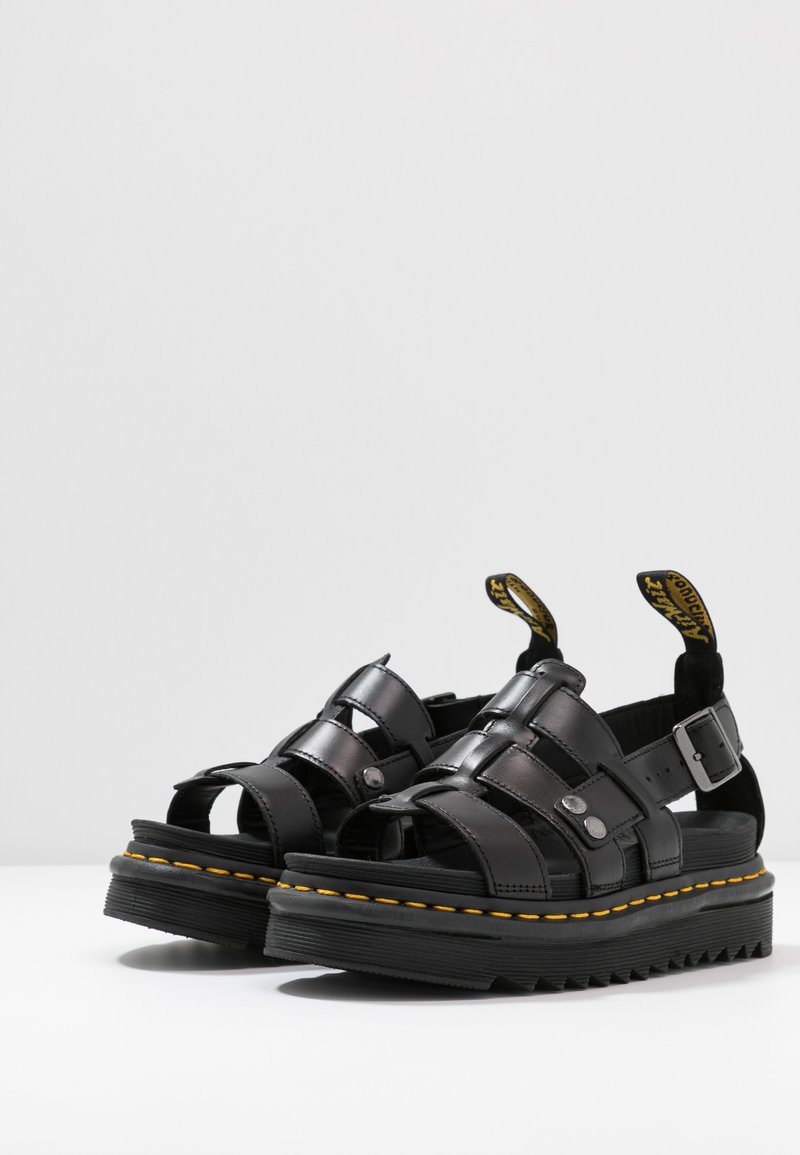 Sandalias de cuero negro con una correa ajustable en el tobillo, plantilla texturizada, costuras amarillas y una suela de goma gruesa con un patrón en zigzag.