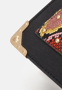 Coin de sac en cuir noir texturé avec un accent en métal doré en forme de cœur. Panneau en imprimé serpent coloré avec des clous dorés.