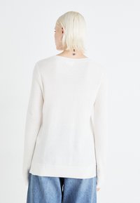 Pull en tricot blanc avec une finition texturée, doté de manches longues et d'un col rond, associé à un jean bleu ample.