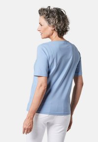 Lichtblauw T-shirt met korte mouwen van zachte stof en een ronde halslijn, gecombineerd met witte broeken. Gladde textuur, eenvoudig ontwerp, geen patronen of accenten.