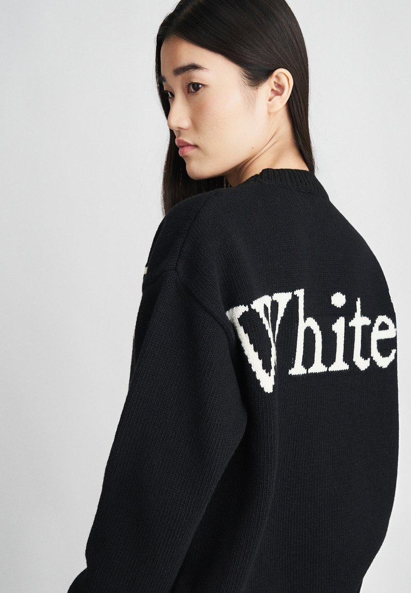 Maglione nero lavorato a maglia con la scritta bianca "White" in evidenza sulla schiena. Il design include un colletto a coste e un tessuto strutturato.